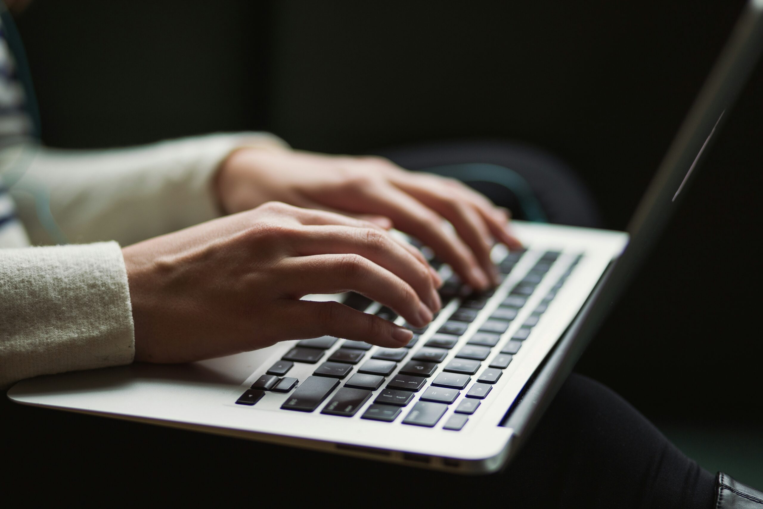 Bildet viser et menneske som sitter ved en laptop og skriver. Det er kun hendene til vedkommende og tastaturet og nederste del av skjermen som er synlig.