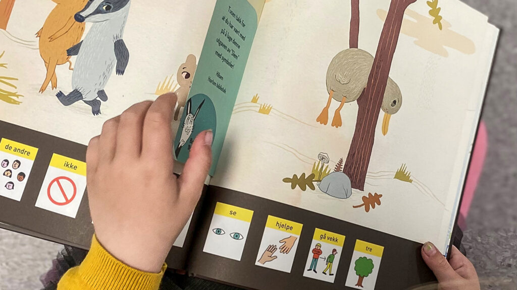 Bildet viser boken 'Slem' som inneholder grafiske symboler. Det er to barnehender synlige som holder i boken.
