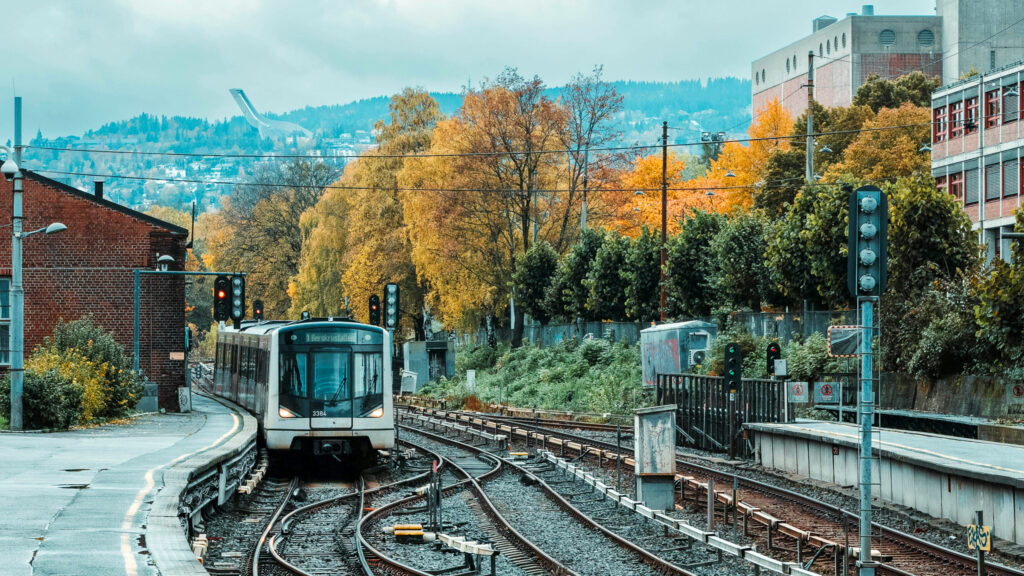 Bildet viser t-banespor ved Majorstua stasjon i Oslo. Det er en t-bane på linja og i bakgrunnen skimtes hoppbakken i Holmenkollens