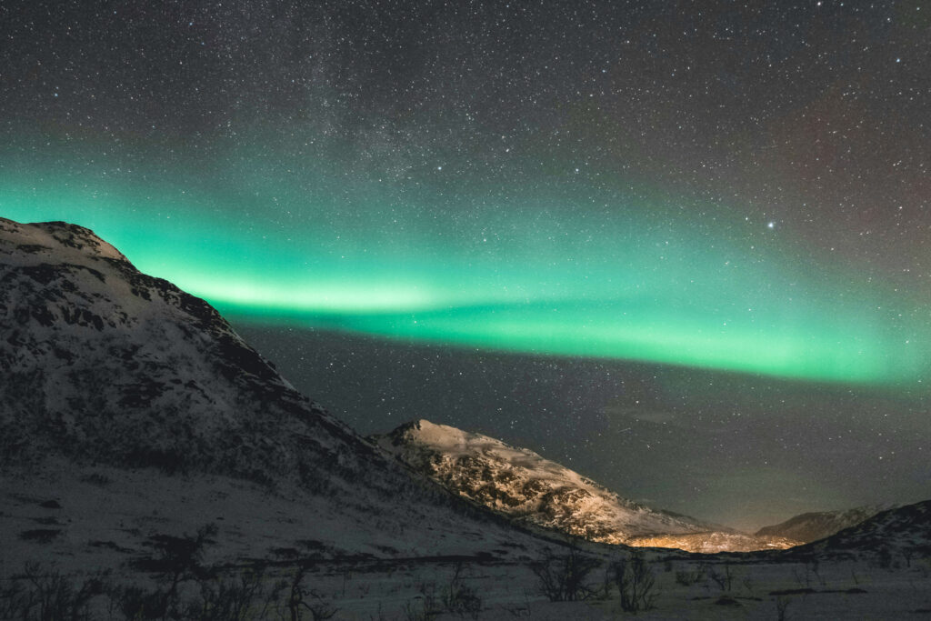 The image shows green nothern lights against a dark, starry sky with mountains below.