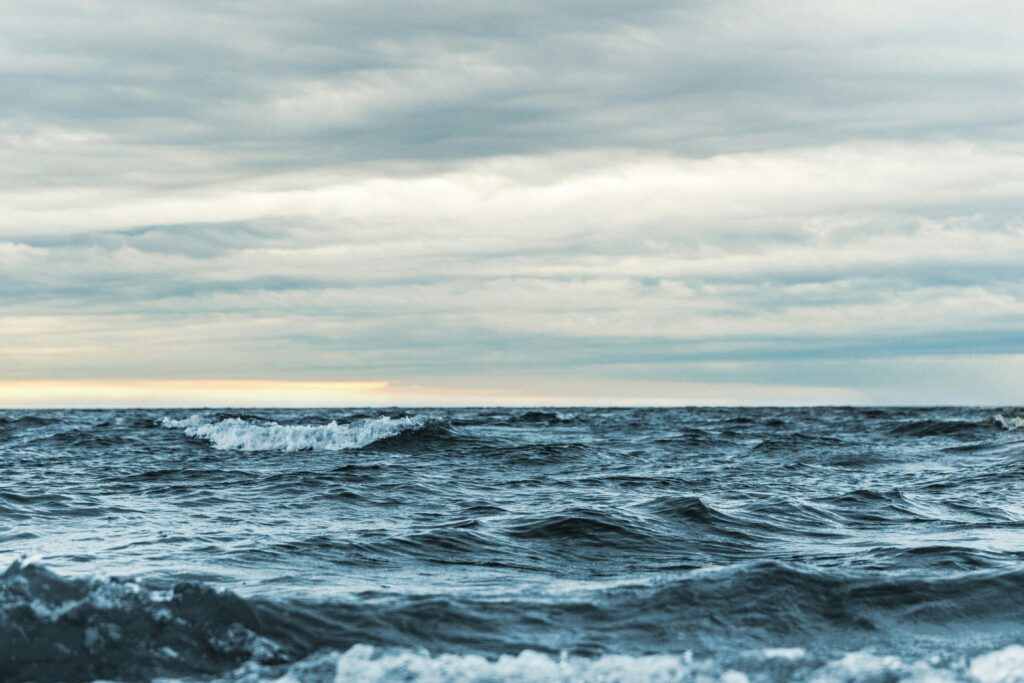 The image shows a cloudy day and a rough sea with crashing waves.