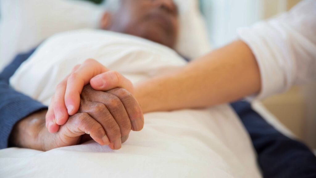 Closeup of a patient holding hands with another person.