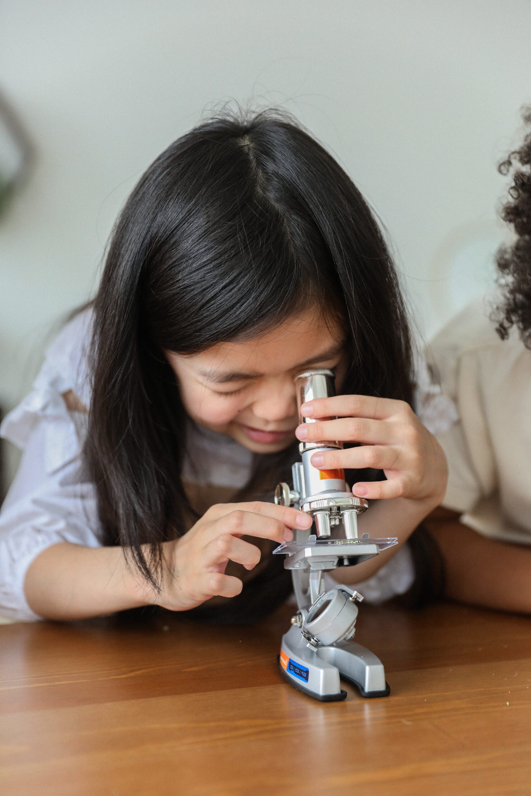 A young girl with black hair is featured looking through a small microscope.