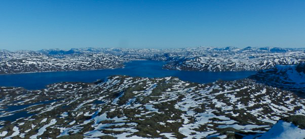 The image shows a sparsely covered snow area in Jotunheimen, Norway. The sky is blue.
