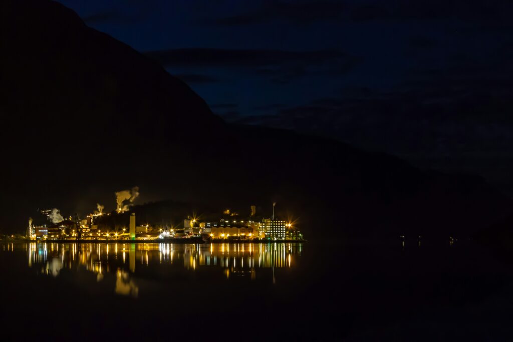 It's night time. A large industrial plant in full lights can be seen across a body of water